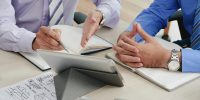 Close-up image of coworkers discussing data on tablet computer screen